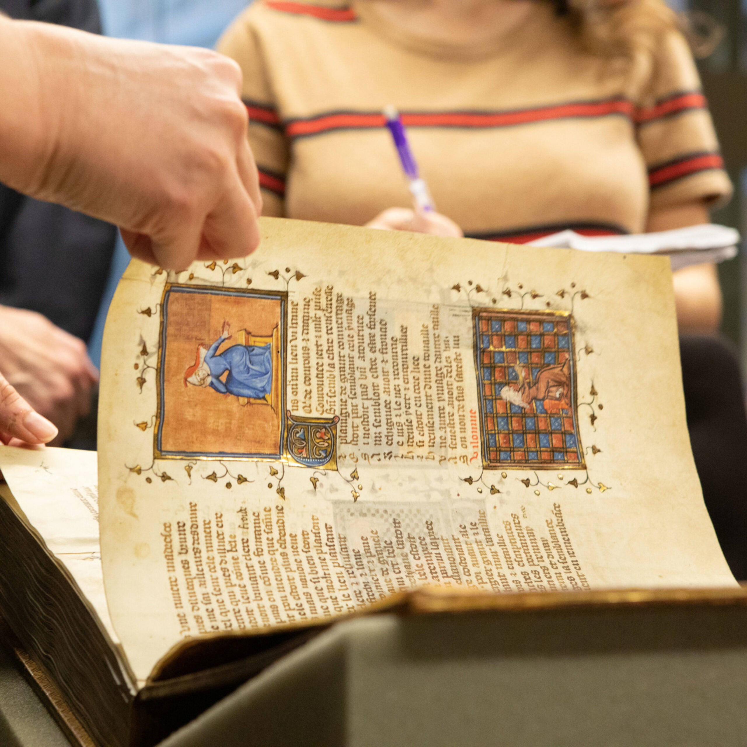 Hand turning page of a book of 13th century poems in Firestone special collections.
