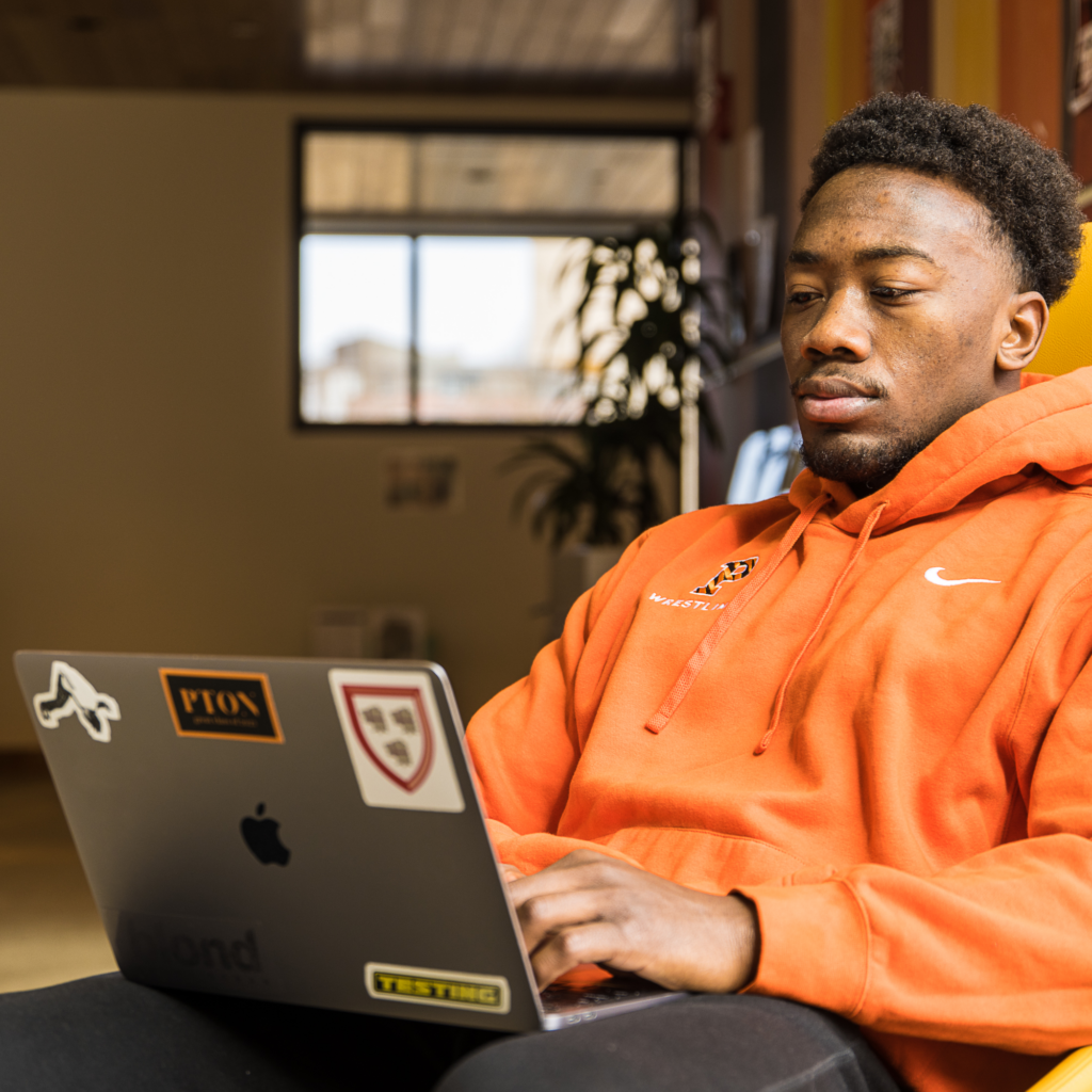 Quincy Monday ‘23 sitting in a chair working on his laptop in the lobby of New College West